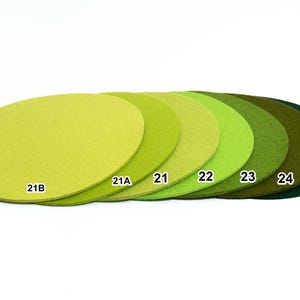 Puede incluir: Una colecci&oacute;n de siete posavasos circulares de fieltro dispuestos en fila, que muestran un degradado de tonos verdes desde el lima claro hasta el verde bosque profundo. Cada posavasos tiene un texto blanco: 21B, 21A, 21, 22, 23, 24 y 26.