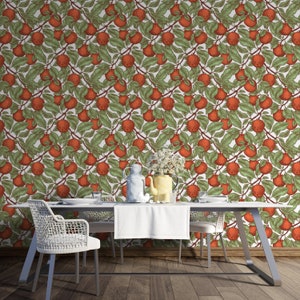 May include: A white dining table with two white chairs and a white tablecloth. The table is set with a white pitcher, a yellow pitcher, and three glasses. The wall behind the table is covered in a wallpaper with a repeating pattern of red apples and green leaves.