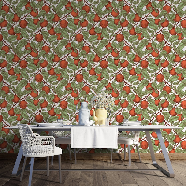 May include: A white dining table with two white chairs and a white tablecloth. The table is set with a white pitcher, a yellow pitcher, and three glasses. The wall behind the table is covered in a wallpaper with a repeating pattern of red apples and green leaves.