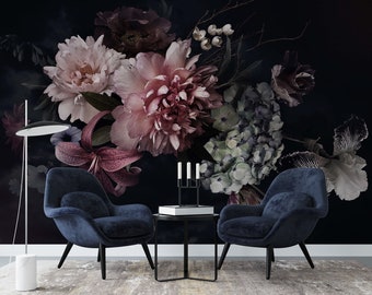 May include: Two dark blue velvet armchairs with black legs face each other in front of a black coffee table with a black candle holder and a book. The chairs are in front of a dark wall with a large floral arrangement of pink, white, and purple flowers.