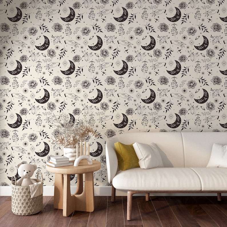 May include: A white sofa with a yellow cushion sits in front of a wall covered in a black and white wallpaper featuring a repeating pattern of moons, flowers, and hands.