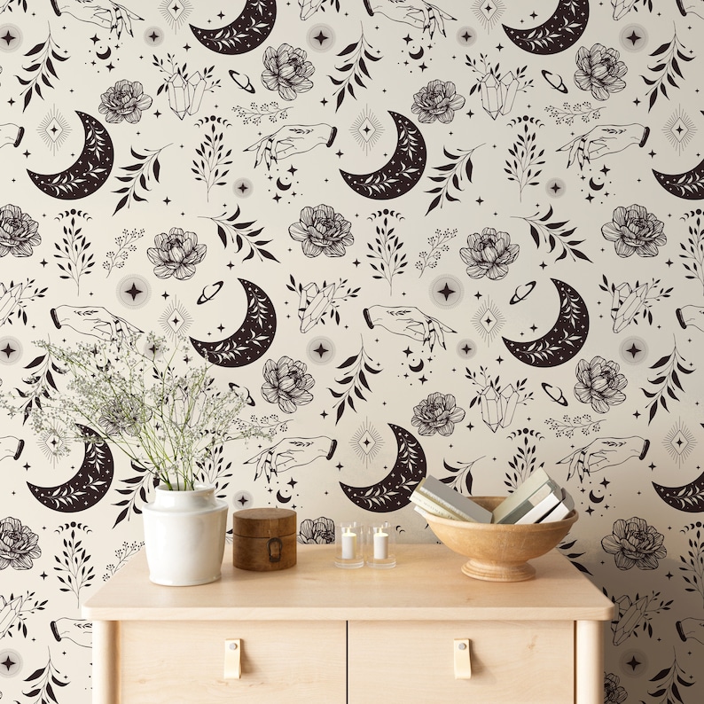 May include: A beige wall with a black and white repeating pattern of moons, stars, flowers, and hands. The pattern is a whimsical and modern design. The wall is decorated with a vase of flowers, candles, and a wooden box.