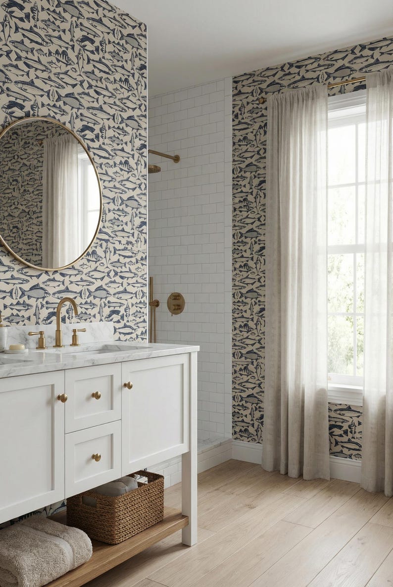 May include: A bathroom with a white vanity, a round gold mirror, and a shower. The walls are decorated with wallpaper featuring a pattern of blue and gray fish. The shower has white subway tiles and gold fixtures.