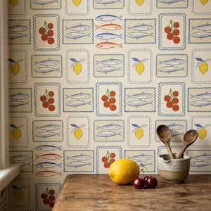 May include: A cream-colored wallpaper with a repeating pattern of sardines, lemons, and cherries in blue, red, and yellow. The design is framed in a blue postage stamp style. Wooden spoons rest in a ceramic bowl on a wooden table.