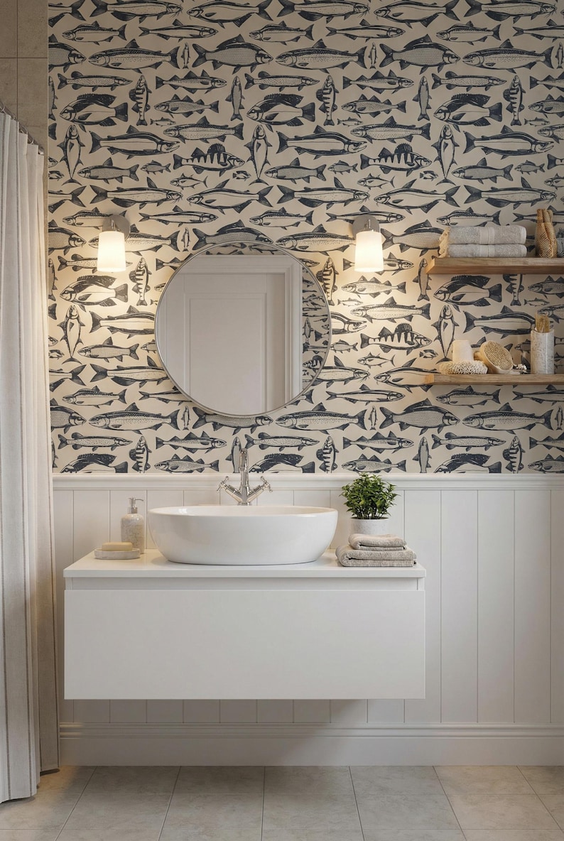 May include: A bathroom with a white vanity, a round mirror, and a fish-patterned wallpaper. The wallpaper features a repeating pattern of blue fish on a cream background. A small plant and towels are on the vanity.