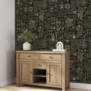 May include: A wooden cabinet with three drawers and two doors. The cabinet is in front of a black and gold wallpaper with a botanical and alchemical design. The wallpaper features illustrations of plants, herbs, and scientific instruments.