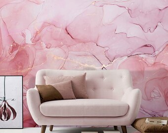 May include: A light pink loveseat with wooden legs and three throw pillows in shades of brown and pink. The background is a pink and gold abstract design. A framed artwork and stacked books are also visible.
