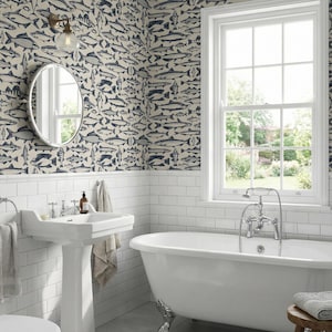 May include: A bathroom with white subway tile, a pedestal sink, and a claw-foot bathtub. The walls are covered in wallpaper with a repeating pattern of blue and gray fish. A round mirror and a window with a view complete the scene.