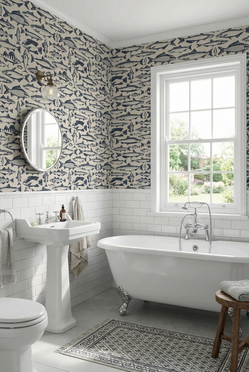 May include: A bathroom with white subway tile, a pedestal sink, and a claw-foot bathtub. The walls are covered in wallpaper with a repeating pattern of blue and gray fish. A round mirror and a window with a view complete the scene.