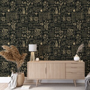May include: A black and gold wallpaper with a repeating pattern of botanical illustrations, including flowers, plants, and herbs. The pattern also includes various symbols, such as stars, moons, and hands. The wallpaper is displayed on a wall in a room with a wooden dresser, a lamp, and a vase with dried flowers.