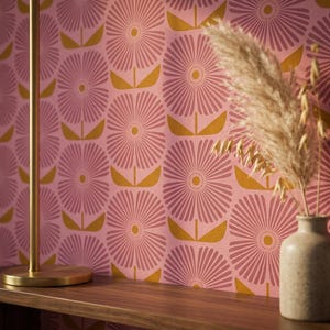 May include: Pink wallpaper featuring a repeating floral design in darker pink and gold. A wooden shelf supports a vase with dried grasses. A gold lamp is visible on the left.
