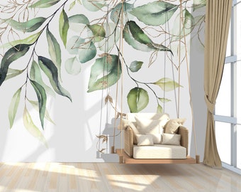 May include: A white hanging chair with cushions, suspended from a ceiling with gold rope, in front of a white wall with a watercolor mural of green leaves and gold accents.