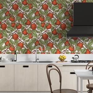 May include: A kitchen with white cabinets and a wood floor. The backsplash is a white wallpaper with a repeating pattern of red apples and green leaves.