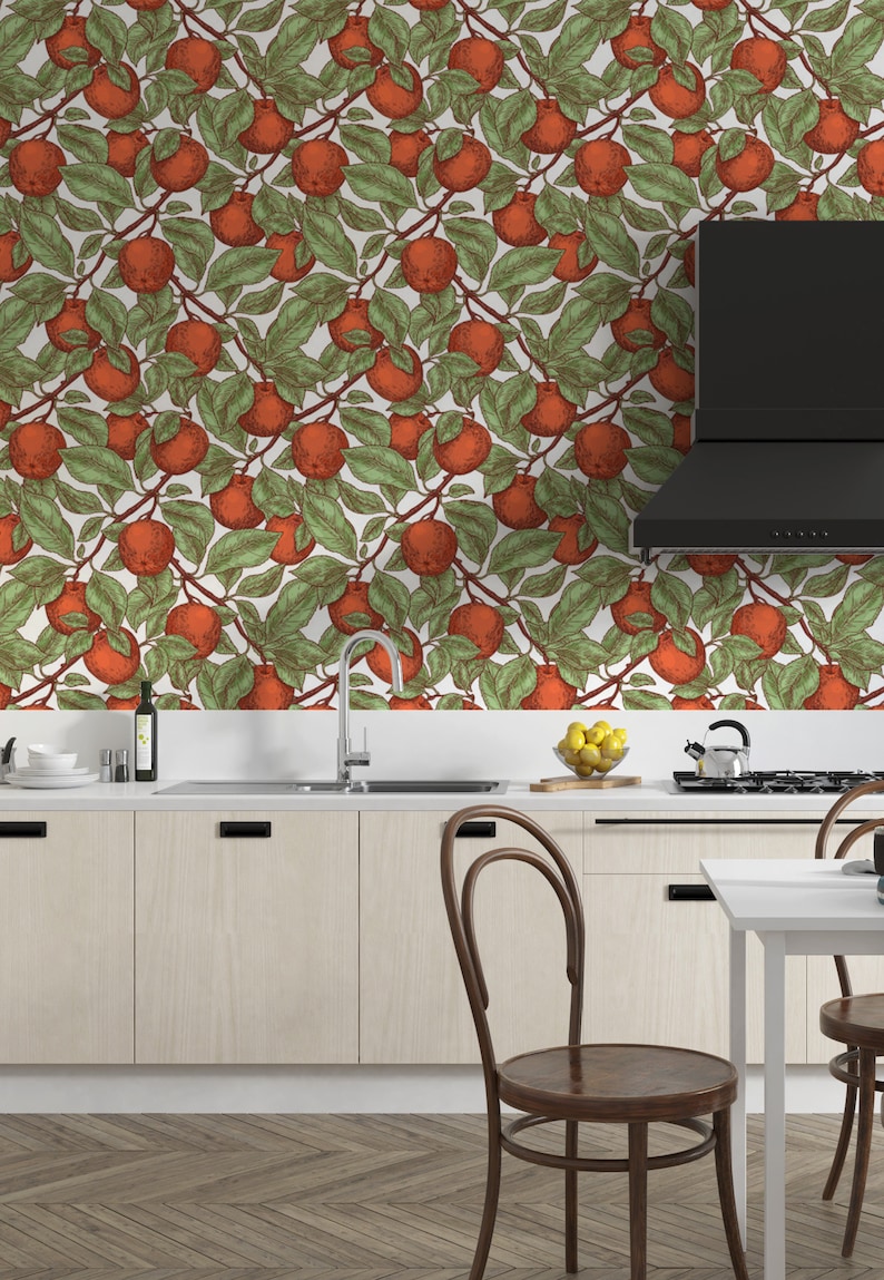 May include: A kitchen with white cabinets and a wood floor. The backsplash is a white wallpaper with a repeating pattern of red apples and green leaves.