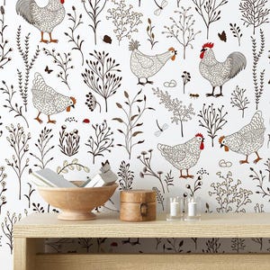 May include: White wallpaper featuring a repeating pattern of chickens, roosters, and botanical elements in brown and black. A wooden bowl, a small wooden box, and candles sit on a light-coloured wooden surface.