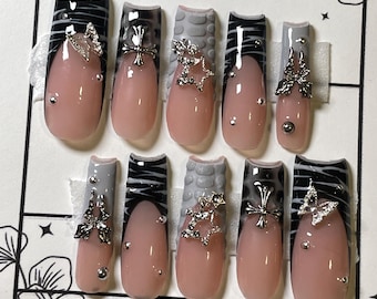 May include: Set of ten false nails with a black and white zebra print, gray textured design, and silver accents. The nails are hand-painted with a variety of designs, including stars, crosses, and butterflies. The nails are labeled "bopha nails" and "handpainted with love by:"