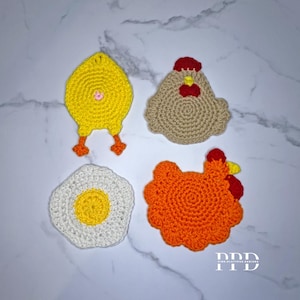 May include: Four handmade crochet items: a yellow chick, a tan hen, a white egg with a yellow yolk, and an orange hen. The chick has orange feet, and the hens have red accents. The items are arranged on a white and gray marble surface.