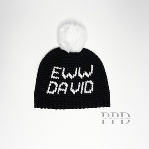 May include: Black crocheted beanie with a white pom pom and the text "Eww David" in white.
