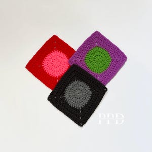 Op de afbeelding: Drie gehaakte vierkanten met verschillende gekleurde cirkels in het midden. De vierkanten zijn rood, paars en zwart. De cirkels zijn roze, groen en grijs.