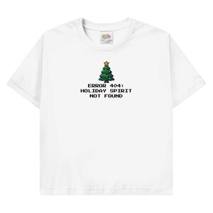 Könnte beinhalten: Weißes T-Shirt mit Rundhalsausschnitt und Grafik eines pixeligen Weihnachtsbaums mit goldenem Stern. Der Text "ERROR 404: HOLIDAY SPIRIT NOT FOUND" ist schwarz und unter dem Baum zentriert.