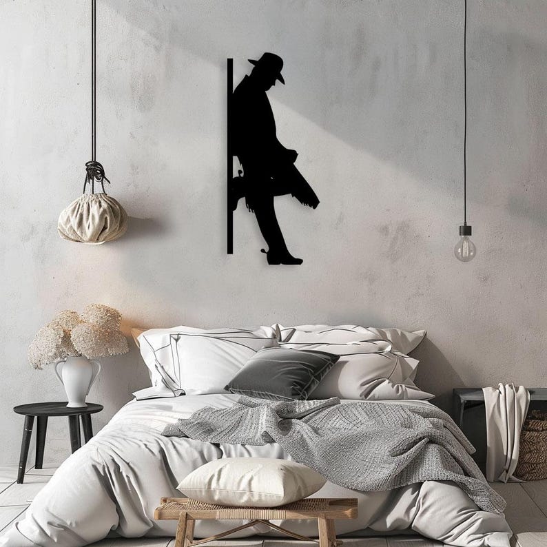 Pu&ograve; includere: Arte da parete in metallo nero a forma di silhouette di una persona con un cappello che si appoggia a un muro. L'opera &egrave; esposta in una camera da letto con un letto, cuscini e una coperta.