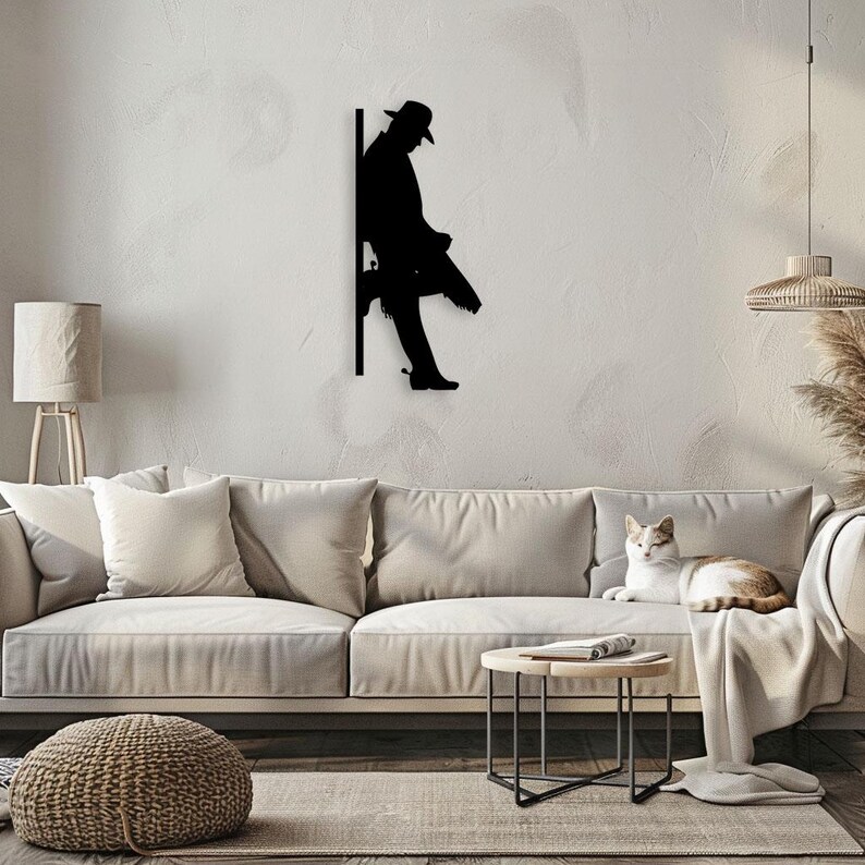 Pu&ograve; includere: Arte da parete in metallo nero a forma di silhouette di una persona con un cappello che si appoggia a un muro. La silhouette &egrave; montata su una parete bianca in un soggiorno.