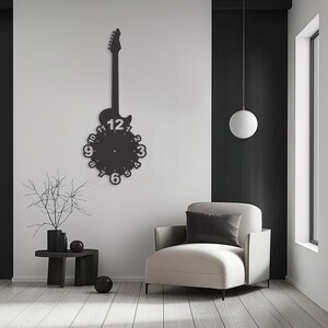 May include: Black electric guitar shaped wall clock with a white face and black numbers. The clock is hanging on a white wall in a room with a white armchair and a small black side table.