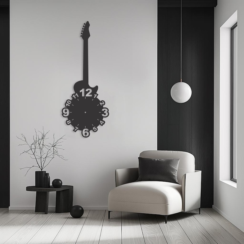 May include: Black electric guitar shaped wall clock with a white face and black numbers. The clock is hanging on a white wall in a room with a white armchair and a small black side table.