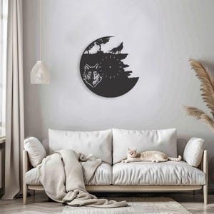 May include: Black and white wall clock with a wolf design. The clock is mounted on a white wall above a white couch. A cat is sitting on the couch.
