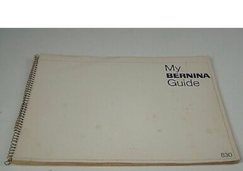 Puede incluir: Un libro encuadernado en espiral de color crema con el t&iacute;tulo "My BERNINA Guide" en texto negro. El libro tiene una encuadernaci&oacute;n en espiral met&aacute;lica en el lado izquierdo y el n&uacute;mero "830" en la esquina inferior derecha.