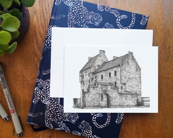 Puede incluir: Un dibujo en blanco y negro a pluma y tinta de un castillo de piedra con una gran entrada arqueada. El dibujo está en una tarjeta blanca con un sobre estampado en azul y blanco detrás.