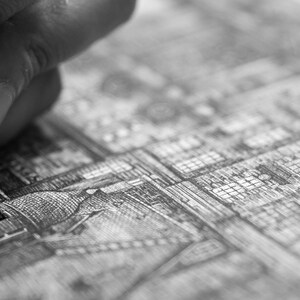 Puede incluir: Imagen en blanco y negro de una mano usando un bol&iacute;grafo de punta fina para dibujar una ilustraci&oacute;n arquitect&oacute;nica detallada. El bol&iacute;grafo est&aacute; en &aacute;ngulo, creando l&iacute;neas y sombreado precisos en el papel. La obra de arte representa una ciudad compleja.