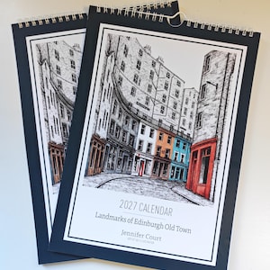 May include: Two spiral-bound 2027 calendars titled Landmarks of Edinburgh Old Town by Jennifer Court. The cover features a black and white ink illustration of city buildings with selective orange and blue color accents on the storefronts.