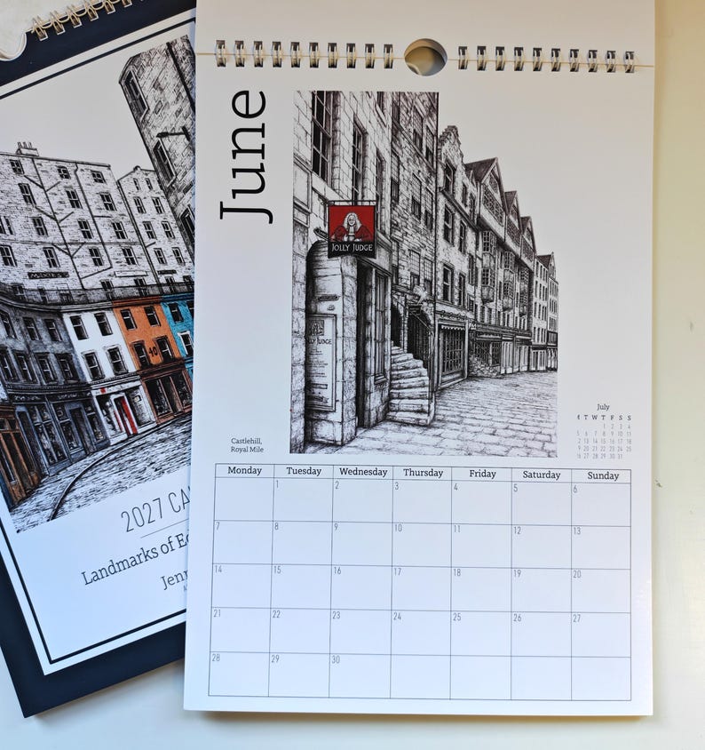 May include: A 2027 wall calendar page for June featuring a black and white ink illustration of Castlehill on the Royal Mile. The page includes a grid for the month, a small July calendar, and a red sign labeled Jolly Judge on a stone building.