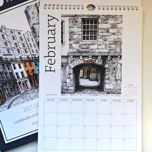 May include: A 2027 wall calendar featuring a black and white ink illustration of Bakehouse Close in Edinburgh for the month of February. The page displays a grid for the month, a small March calendar, and a detailed stone archway drawing.
