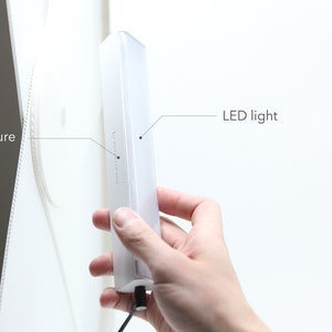 May include: A white LED light with a magnetic structure. The light is attached to a white surface.