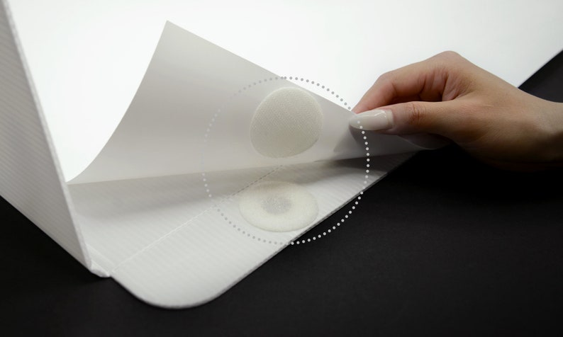 May include: Two white adhesive dots are attached to a white surface. The adhesive dots are being peeled off the surface.