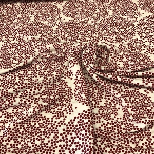 Könnte beinhalten: Weißer Stoff mit rotem Punkte-Muster. Die Punkte sind in einem wirbelnden, floralen Design angeordnet.
