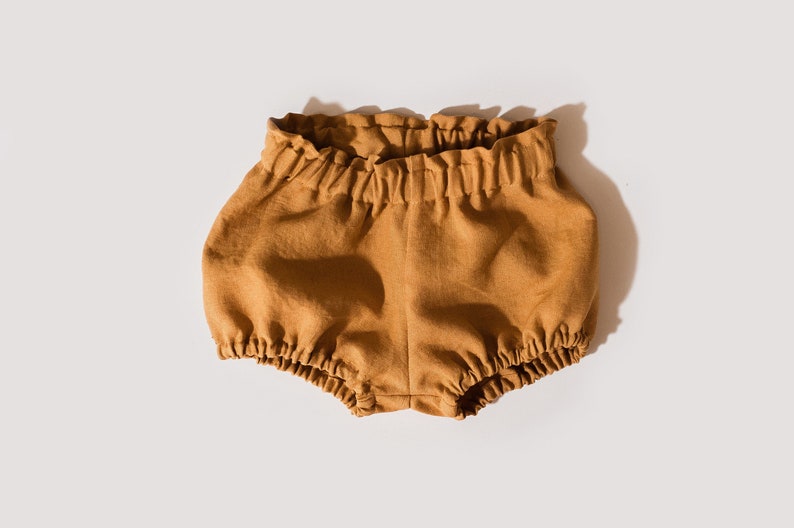 May include: A pair of brown linen baby bloomers with a gathered elastic waistband.