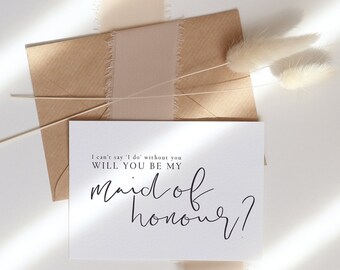 May include: A white card with the text "I can't say 'I do' without you. Will you be my maid of honour?" written in black calligraphy. The card is on a brown envelope with a beige ribbon.