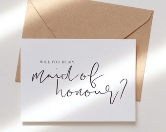 May include: A white card with black text that reads "Will you be my maid of honour?" The card is sitting on a brown envelope.