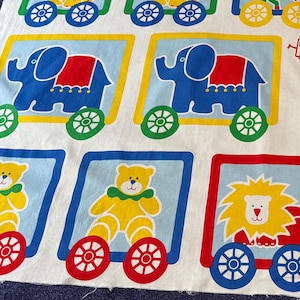 May include: A white fabric panel with the text "Animal Crackers Wall Hanging" printed in black. The panel features nine colorful squares, each containing a different animal on a train car. The animals include a lion, elephant, tiger, horse, and teddy bear. The panel includes instructions for making the wall hanging.