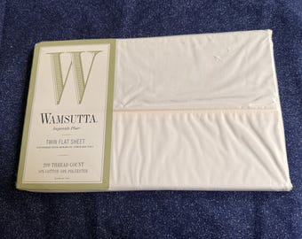 May include: A white Twin flat sheet in its original packaging. The packaging features the brand name "Wamsutta" and product details. The sheet is made of 50% cotton and 50% polyester with a 200 thread count.