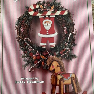 May include: A Christmas-themed book cover with the text "Jolly Christmas Day." The cover features a wreath with a Santa Claus figure holding a candy cane, and a wooden rocking horse. Designed by Betty Headman.