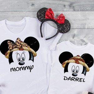 May include: White t-shirts featuring a Mickey Mouse design. One shirt says "mommy" and the other says "Darrel". The Mickey Mouse design includes a safari hat and a bow. A pair of Minnie Mouse ears and two Mickey Mouse plush toys are also in the image.