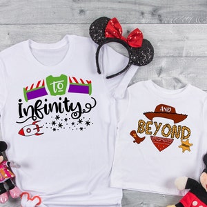Puede incluir: Dos camisetas blancas con temática de Toy Story. La camiseta más grande dice "to infinity" con un cohete y estrellas. La camiseta más pequeña dice "and beyond" con un sombrero de vaquero, un pañuelo y botas.