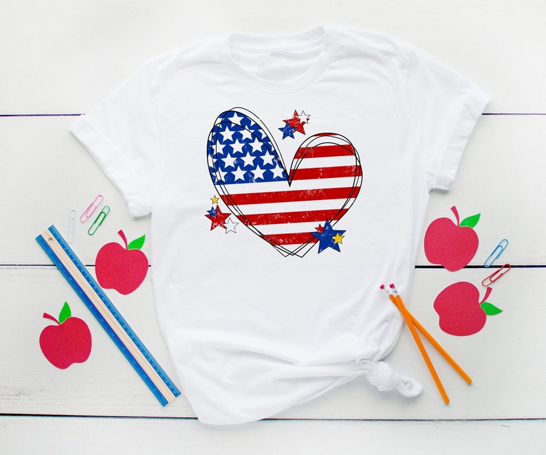 May include: White t-shirt with a red, white, and blue heart-shaped American flag design. The flag is distressed and has stars around it.