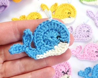 May include: A collection of crocheted whale appliques in various colors, including blue, green, yellow, pink, and purple. The whales are all approximately the same size and have a simple, whimsical design.