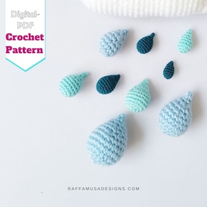 Può includere: Una collezione di gocce di pioggia all'uncinetto in varie tonalità di blu e verde. Le gocce di pioggia sono disposte su una superficie bianca. Il testo "Digital-PDF Crochet Pattern" è visibile nell'angolo in alto a sinistra dell'immagine.