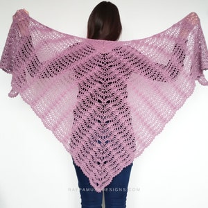 Puede incluir: Un chal delicado y de encaje en un suave tono morado. El chal está tejido a ganchillo con un patrón delicado y tiene un borde festoneado.